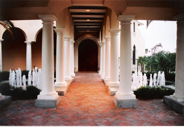 A collegiate outdoor walkway flanked with columns and two bubbling water fountains.