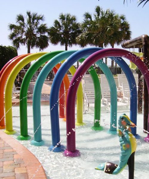 A series of rainbow colored tubes in a line to create a tunnel with soft sprays of water inside to delight children.