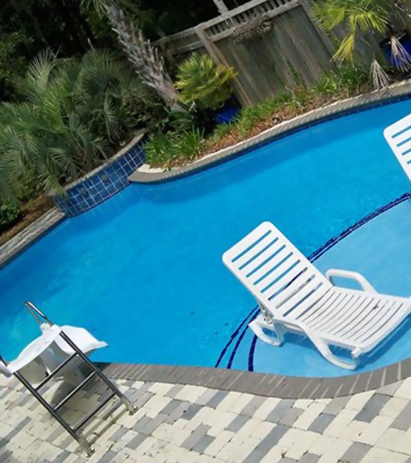 A residential pool with a slide situated nearby and with a shallow wading area with damped lounge chairs.